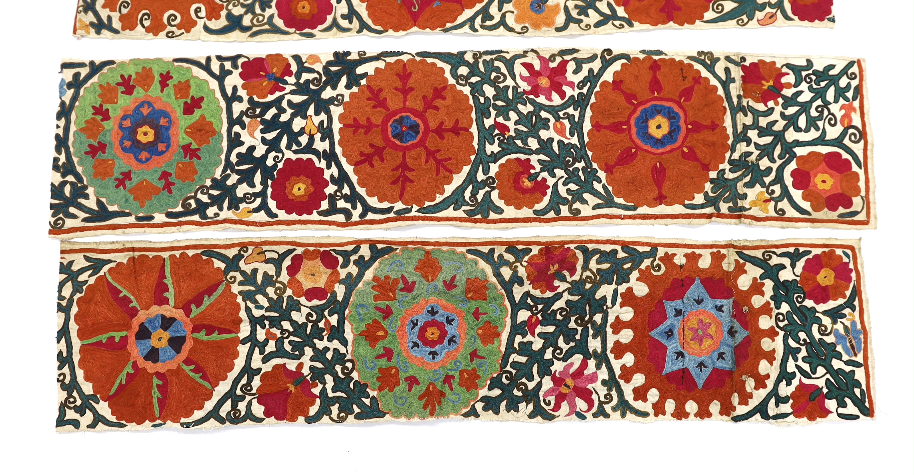 Four early 20th century Uzbek Suzani panels, embroidered with hand dyed silk on thick woven linen, in large brightly multi-coloured symbolic motifs, possibly embroidered for a larger prayer rug or hanging, longest 125cm